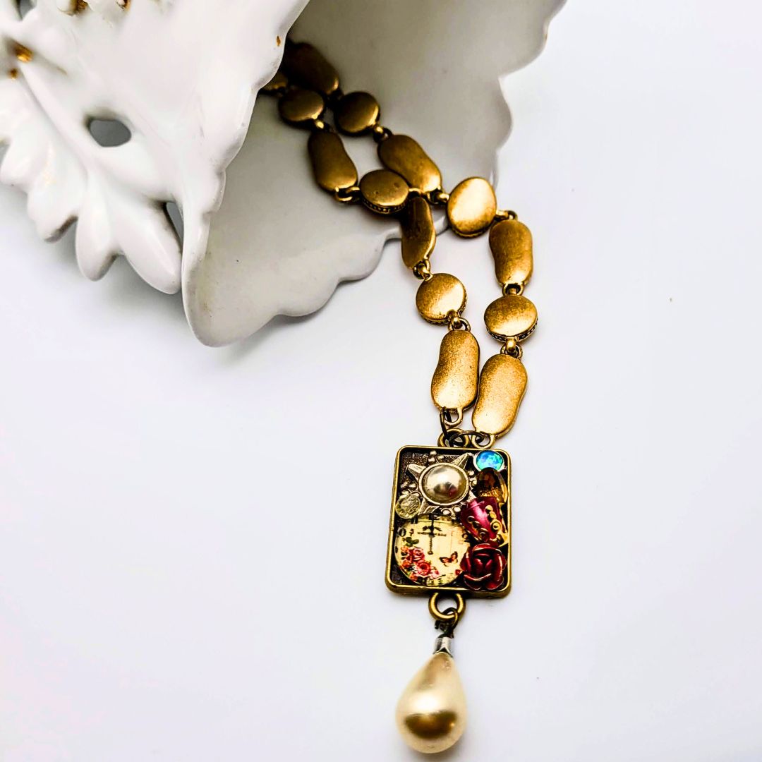 The collage pendant is inlaid with a selection of modern and vintage jewelry pieces and beads with a classical pearl drop. High-quality brushed gold chain which adds to the charm of this piece.